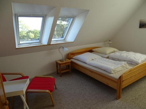 a bedroom with a bed and a chair and two windows at Der Ferienhof am Meer in Fehmarn
