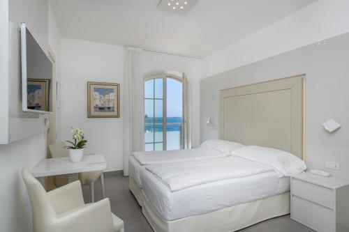 a white bedroom with a bed and a desk and a chair at Hotel Vega in Malcesine