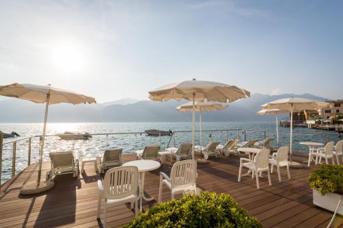 a deck with chairs and tables and umbrellas on the water at Hotel Vega in Malcesine
