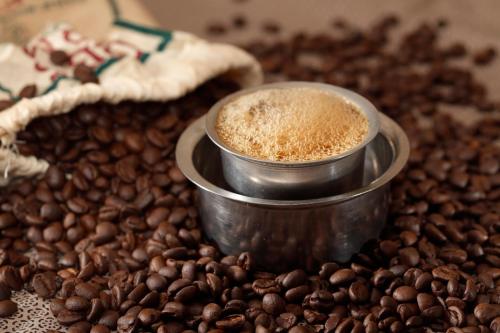 a cup of coffee sitting on a pile of coffee beans at Hotel Sri Hayagriva in Srīrangam