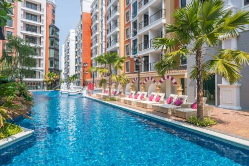 uma piscina com cadeiras, palmeiras e edifícios em ESPANA Pattaya by Plearn em Praia de Jomtien