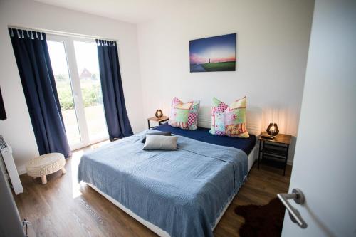 Schlafzimmer mit einem Bett mit blauer Bettwäsche und einem Fenster in der Unterkunft Strandchalet Elmo II in Wremen