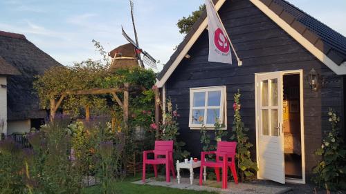 a black house with red chairs and a table and a windmill at Zalk blijven slapen in Zalk