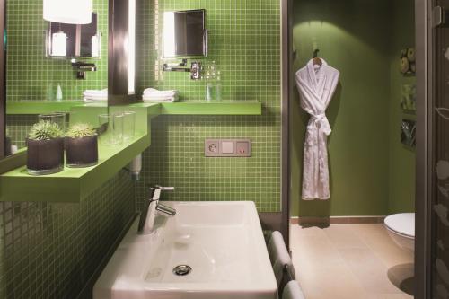 a green bathroom with a sink and green tiles at Mövenpick Hotel München-Airport in Hallbergmoos
