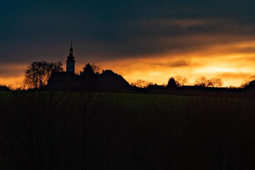 a sunset with a clock tower in a field at Residence Safari Resort - Bison Lodge in Borovany