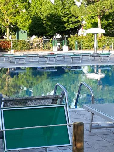 a swimming pool with benches and a table and water at Appartamento Ai Tigli in Caorle