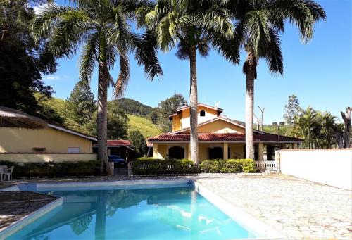 a house with palm trees in front of a swimming pool at Recanto do Ribeirão in Pindamonhangaba