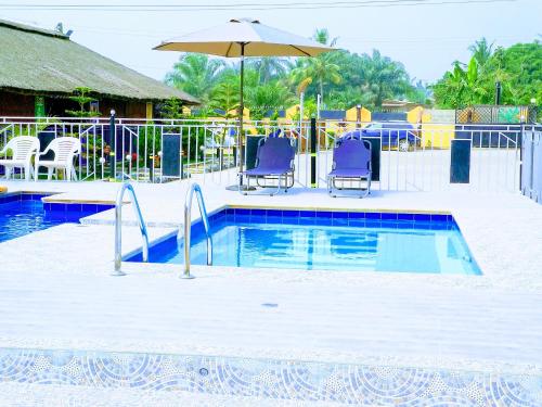 a swimming pool with two chairs and an umbrella at Kikis Court Resort in Hohoe