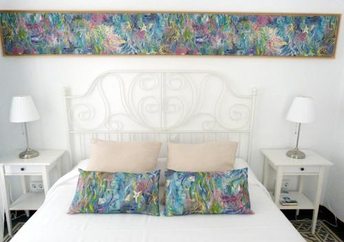 塞维利亚Rodo Arenal的一张带两个枕头的白色床和墙上的绘画