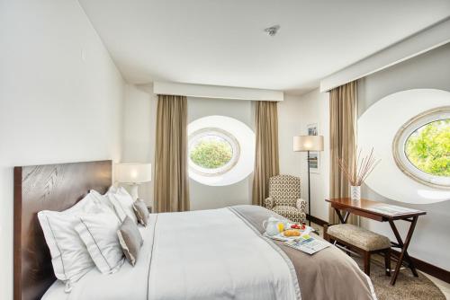 a bedroom with a bed and a desk and two windows at Pateo dos Solares Charm Hotel in Estremoz