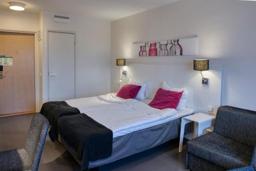 um quarto com uma cama com duas almofadas vermelhas e uma cadeira em Teatterihotelli Riihimäki em Riihimäki