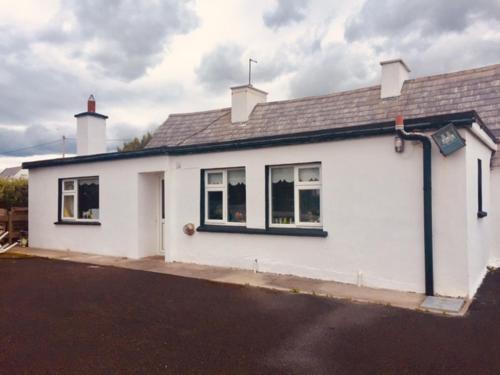 a white house with black windows on a street at Maisie's Seaside Cottage in Quilty