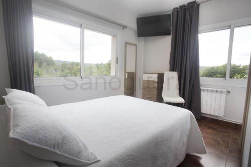 a bedroom with a white bed and two windows at Pensión CHE in O Pedrouzo