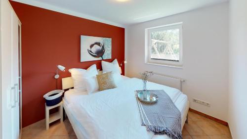 a bedroom with a white bed with a red wall at Feriendorf Südstrand Haus 09 in Pelzerhaken