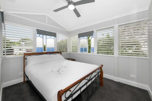 a bedroom with a bed with white sheets and windows at Beautiful Queenslander in Townsville