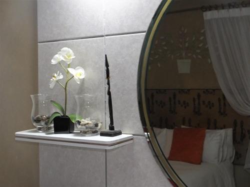 a mirror in a bathroom with a vase with white flowers at Tatenda Guest House in Hazyview