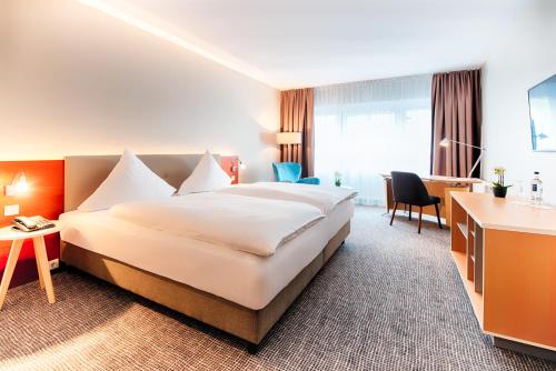 マールブルク・アン・デア・ラーンにあるウェルカム ホテル マールブルクの大きなベッドとデスクが備わるホテルルームです。