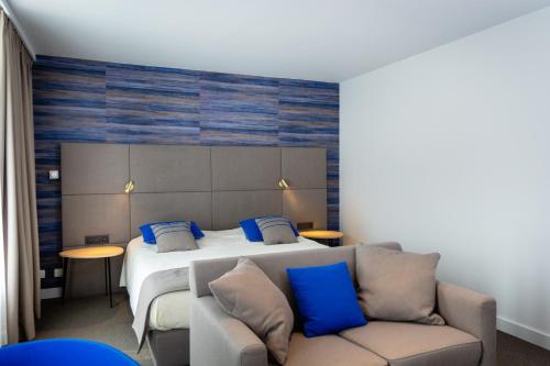 een slaapkamer met een bed met blauwe kussens en een bank bij Hotel Les 3 Cles in Gembloux