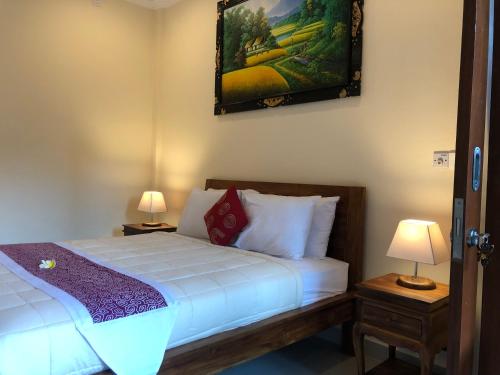 1 dormitorio con 1 cama con 2 lámparas y una pintura en la pared en Taman Indah Homestay, en Ubud