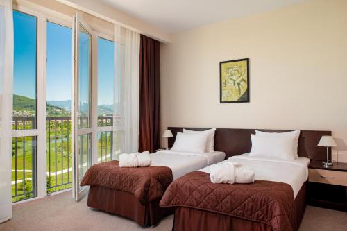 two beds in a hotel room with large windows at Barkhatnye Sezony Sportivny Kvartal Resort in Adler