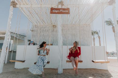 two women sitting on a swing on the beach at Meraki Resort - Adults Only in Hurghada