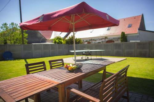 a picnic table with a red umbrella and a bowl of fruit at Apartman Szanyi in Bük