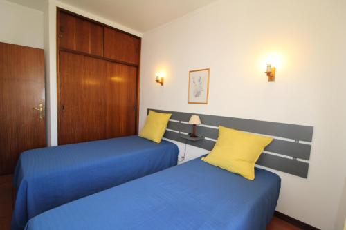 two beds in a room with blue sheets and yellow pillows at ApartamentoSolPraia - BeloHorizonte in Portimão