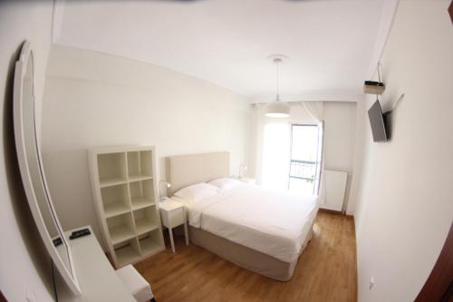 a white bedroom with a bed and a window at Cozy Penthouse in Thessaloniki