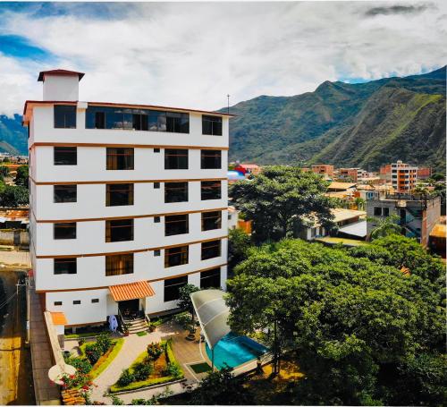 a white building with trees and mountains in the background at Gran Hotel Panorama in Quillabamba