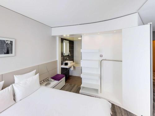 a bedroom with a white bed and a small bathroom at Novotel Suites Luxembourg in Luxembourg