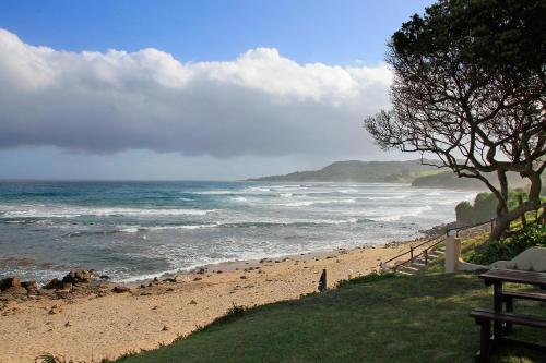 a beach with a bench next to the ocean at Neptunes Cove in Kei-mouth Village
