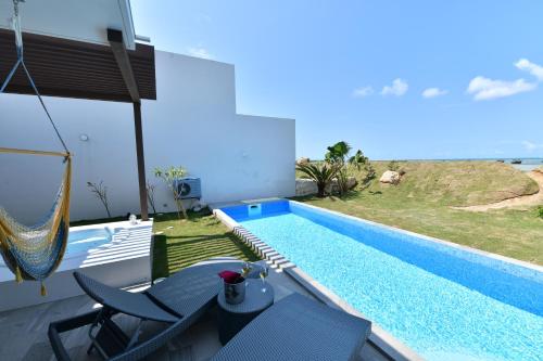 a swimming pool with chairs and a hammock next to a house at Feliz Villa Suite Irabujima Sawada in Miyako-jima
