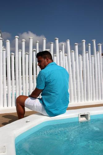 a man sitting on a fence next to a swimming pool at Annio studios in Plaka