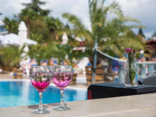 two wine glasses sitting on a table next to a pool at Smartline Meridian Hotel in Sunny Beach