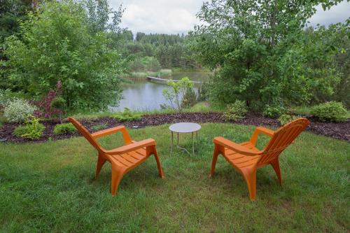 three chairs and a table in the grass near a lake at Dzeņi in Amatciems