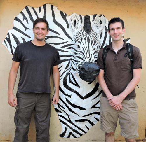 two men standing in front of a zebra painting at Kruger Inn Backpackers in Marloth Park