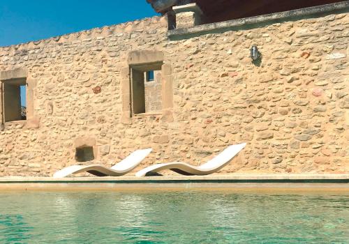 a stone building with white chairs sitting next to the water at Les Toiles du 15 in Montaren-et-Saint-Médiers
