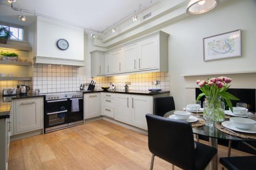 a kitchen with white cabinets and a table with flowers on it at Stunning Royal Crescent Apartment with 3 Bedrooms in Bath