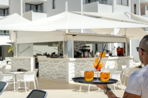 un hombre sosteniendo una bandeja con dos bebidas. en Apartamentos Vibra Jabeque Soul-3SUP en Ibiza