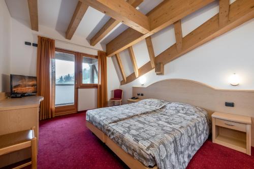 um quarto com uma cama, uma televisão e janelas em Hotel Europa em Pozza di Fassa