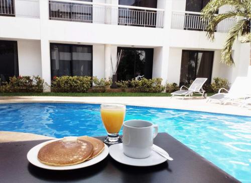 a glass of orange juice and a plate of food next to a pool at Hotel Holly in Mérida