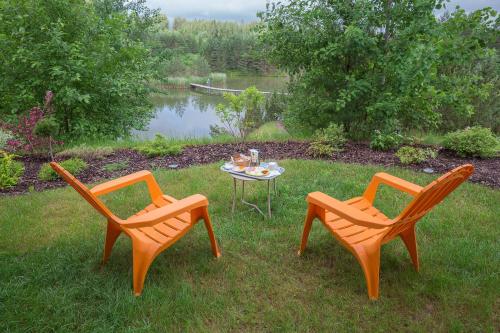 two chairs and a table in the grass near a lake at Dzeņi in Amatciems