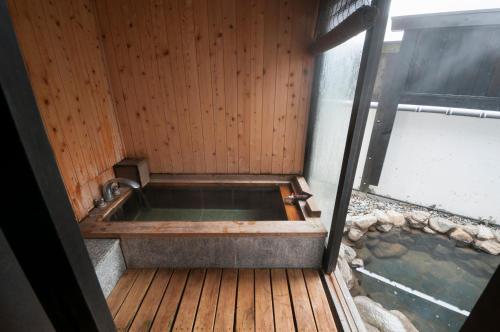 bañera en una terraza de madera con una masa de agua en Okada Ryokan Warakutei, en Takayama