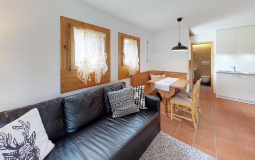 ein Wohnzimmer mit einem schwarzen Ledersofa und einer Küche in der Unterkunft Maurus A4 in St. Moritz