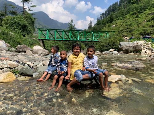 three children sitting on a rock in a river at DreamLand Home stay (JALORI PASS) in Shoja