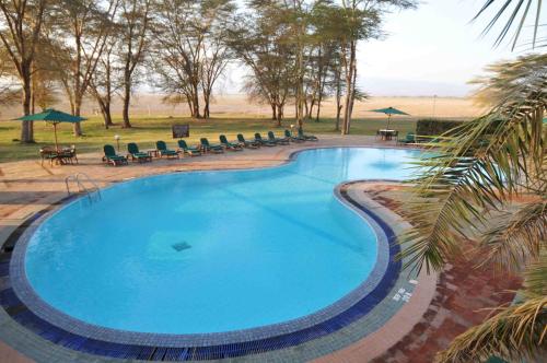 a large blue swimming pool with chairs and umbrellas at Ol Tukai Lodge Amboseli in Amboseli