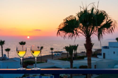two glasses of wine sitting on a table with the sunset at Villa Margo by the Sea in Paphos City