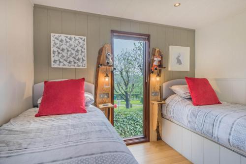 two beds with red pillows in a room with a window at Dobby Lodge in Bassenthwaite