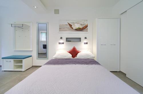 a white bedroom with a large bed with red pillows at Apartments Stolfa in Krk