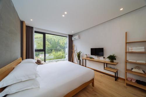 a bedroom with a large white bed and a window at Moganshan Pinhouwu Hotel in Deqing